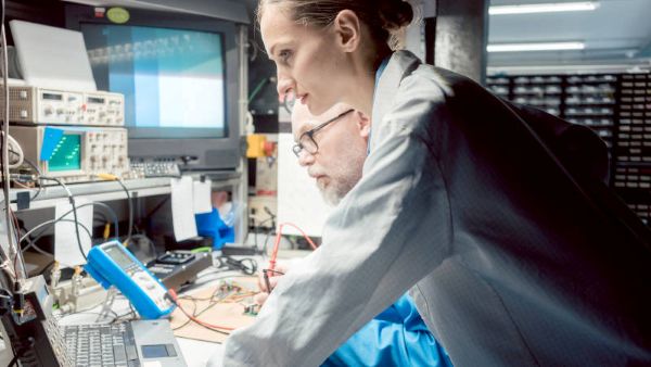 医療機器ODMサービス・モジュール開発のイメージ図。電子機器や測定器が並ぶ作業台で、2人の作業者が作業している様子。